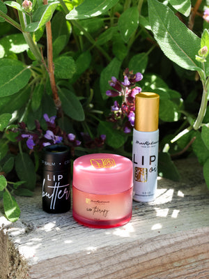 Three lip care products on a wooden surface with greenery in the background