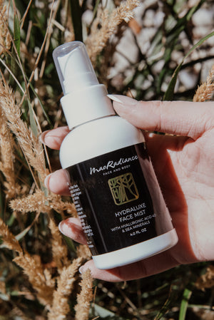 Hand holding a bottle of Mao Radiance Hydraluxe Face Mist against a natural background