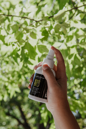 Hand holding a spray bottle with a green leafy background