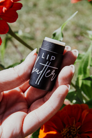 Lip butter stick held in a hand with red flowers in the background